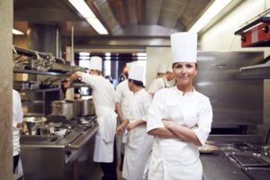 Restaurant Chef posing in her kitchen with two chefs working behind her