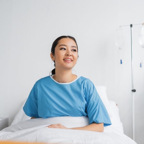 Joyful,Asian,Woman,In,Hospital,Gown,Sitting,On,Bed,In Joyful,Asian,Woman,In,Hospital,Gown,Sitting,On,Bed,In